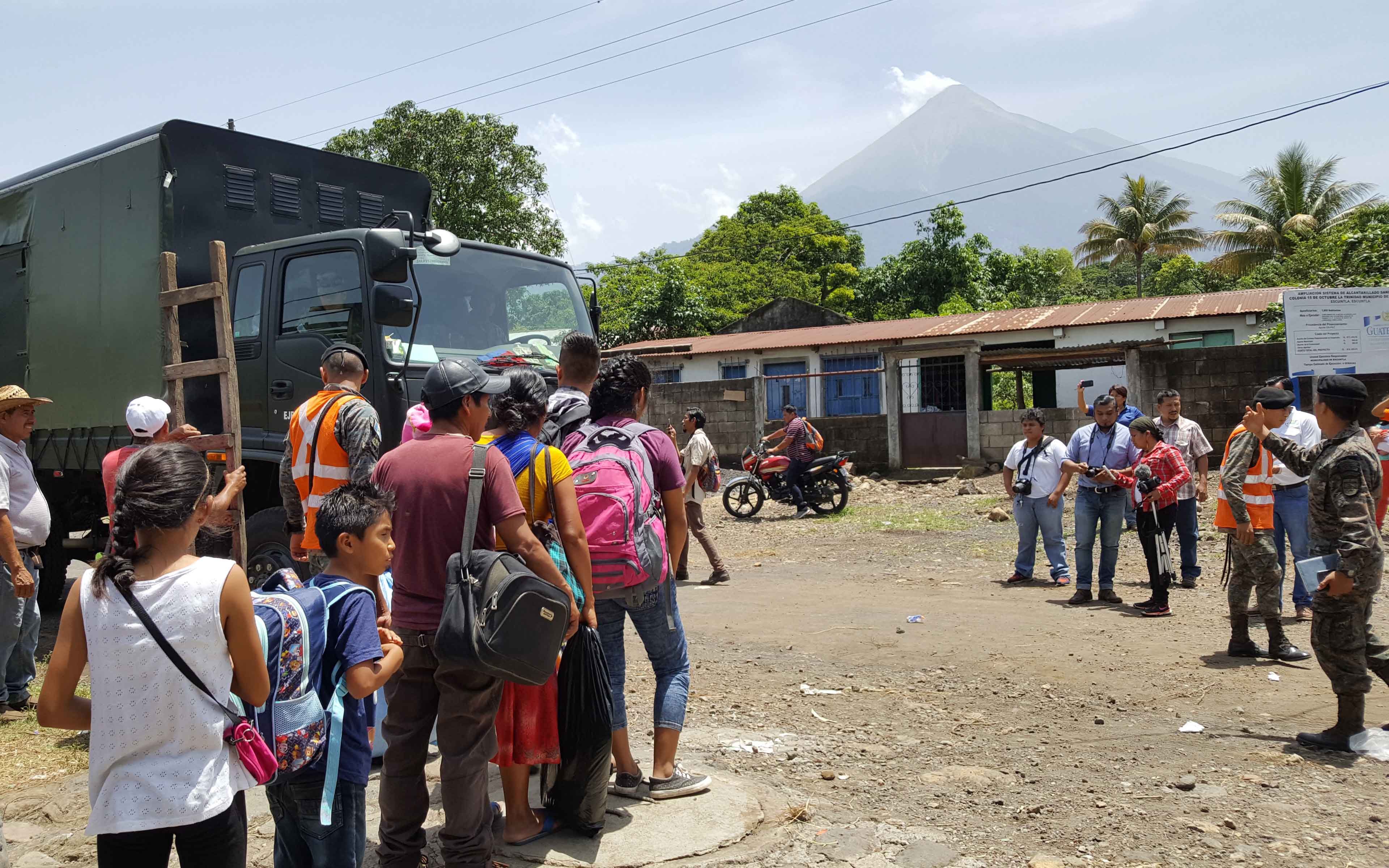 As steam blows out of the top of Fuego in the background, community members of La Trinidad prepare to board army trucks that will evacuate them to temporary shelter in the nearby city of Escuintla.