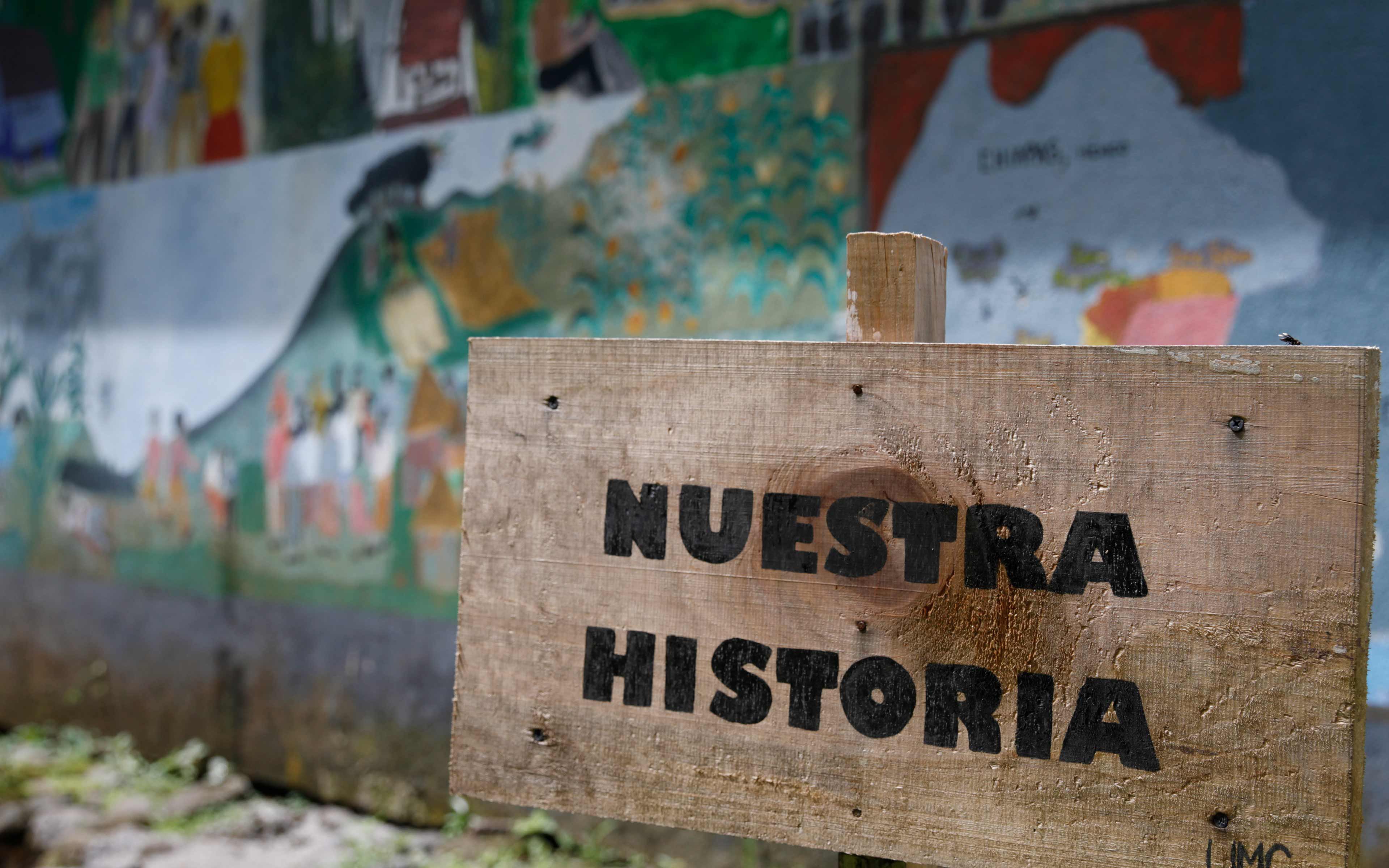 “Our Story:” A sign in front of mural depicting the tragic history of the community in La Trinidad, from a peaceful indigenous Maya village in the western highlands, to conflict and displacement to Mexico in the 1980s, and finally to repatriation and resettlement in Escuintla after the 1998 Peace Accords.