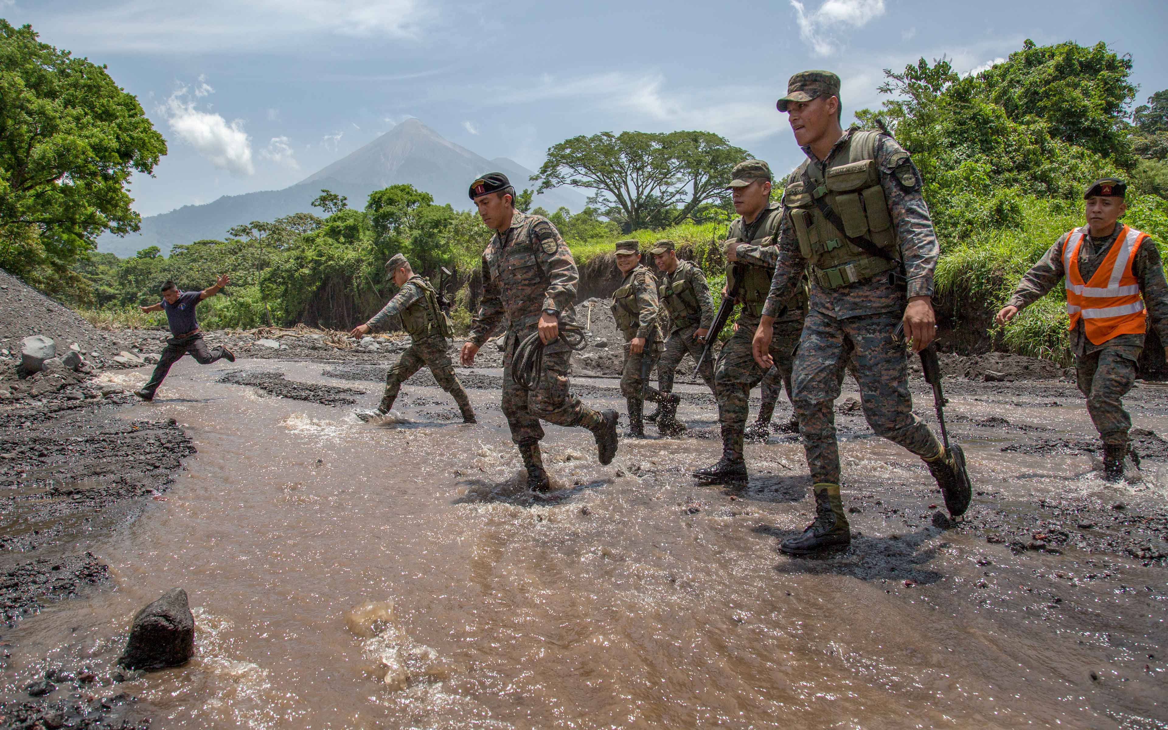 Soldiers walk across a stream amidst volcanic rock and ash and other debris near the community of La Trinidad on the southern slope of Fuego