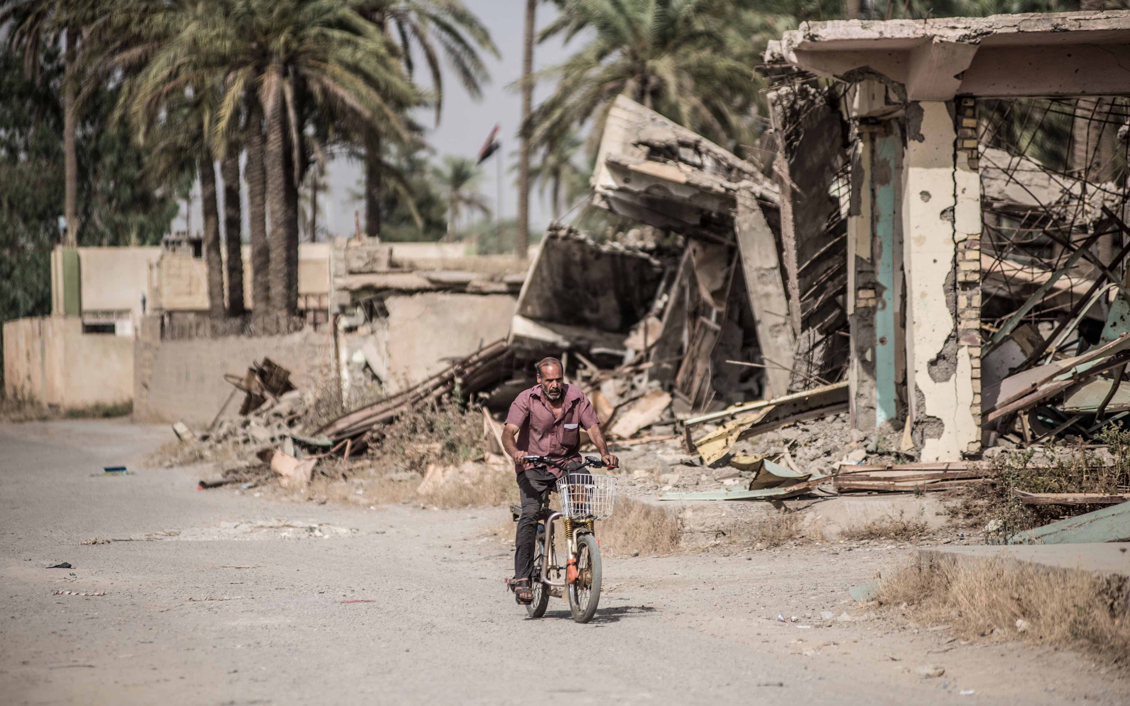 With wreckage around him, a man cycles down the main street of Saadiya. The Iraqi town was largely abandoned after ISIS occupied it in 2014. Though it has now been reclaimed, many residents still have not returned.