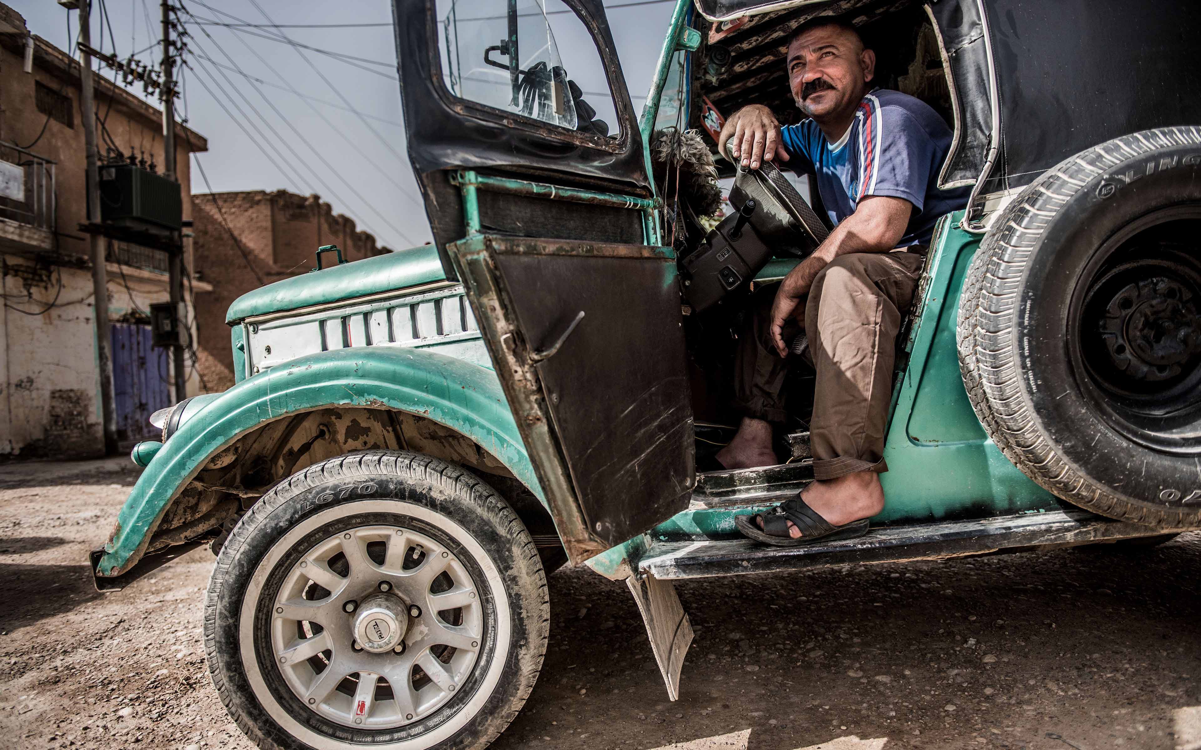 Ghasan Ali, whose name has been changed to protect his identity, sits inside his taxi in the Iraqi town of Saadiya. Though ISIS no longer occupies the community, many residents still have not returned and customers needing rides are infrequent.